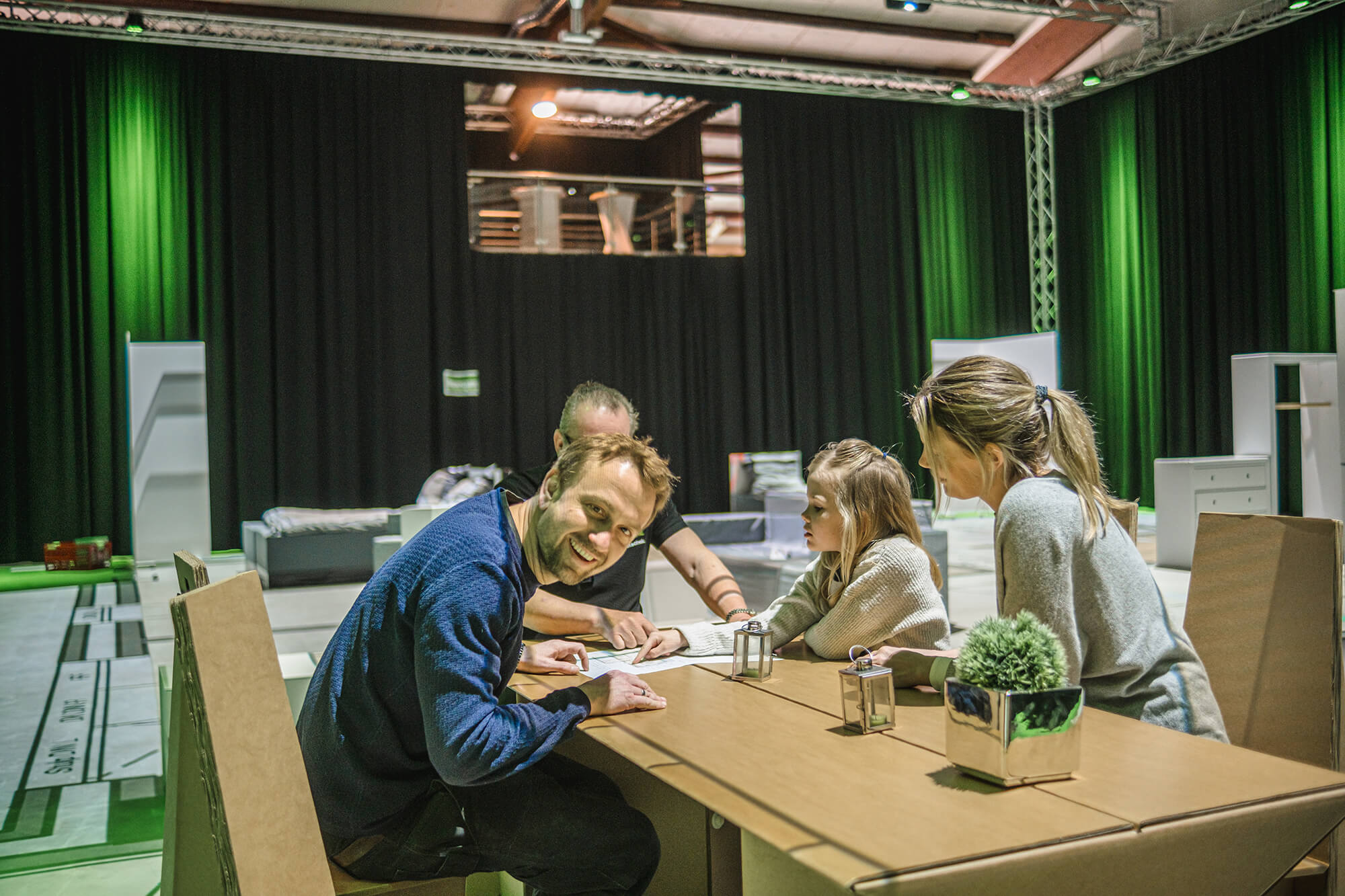Walk your Home in Schleswig-Holstein; Familie sitzt mit Mitarbeiter Ingo am Planungstisch, Mann grinst in die Kamera